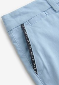 I pantaloni in cotone di colore azzurro chiaro presentano una vestibilità dritta con una texture liscia. Un'etichetta blu scuro con la scritta "BAKER BY TED BAKER" sottolinea la vita.