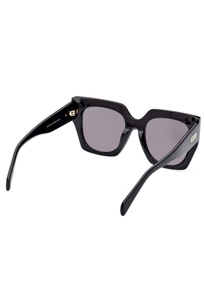 Sorte plastik solbriller med en geometrisk ramme, grå linser og blanke sorte arme. Har et guldaccent nær hængslet.