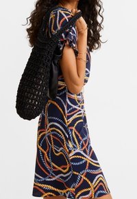 Černá tkaná kabelka přes rameno, doplněná krátkým rukávem šaty s barevným vzorem lana na námořnickém pozadí.