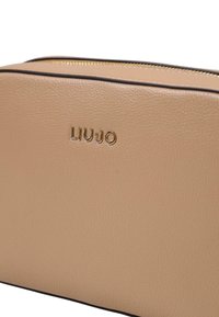 Bolso de cosméticos de cuero beige con acabado texturizado, logo dorado "LIU•JO", cierre de cremallera y ribete marrón contrastante a lo largo de los bordes.