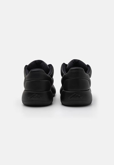 Baskets noires avec une finition en cuir lisse, de forme arrondie, avec un col rembourré et une semelle texturée. Présente un logo discret au niveau du talon.