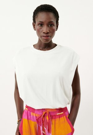 Haut sans manches blanc à côtes avec un col rond, associé à un pantalon à motifs vibrants rose et orange avec une taille à cordon.