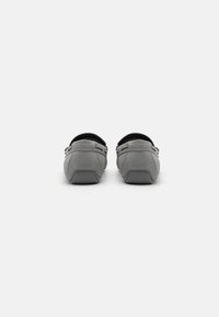 Chaussures en suede gris avec un bout arrondi, semelle en caoutchouc plate et doublure intérieure noire ; elles affichent un design minimaliste avec des accents décoratifs sur les côtés.