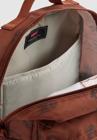 Intérieur d'un sac à dos en tissu marron avec une doublure gris clair et une pochette rembourrée pour ordinateur portable. Présente une étiquette avec "Levi's San Francisco."