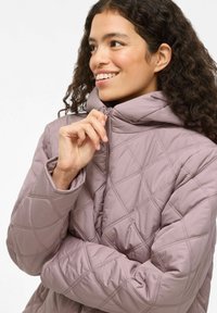 Suaugusiųjų, pūkinė striukė su gobtuvu švelnios mauve spalvos. Ypatybės: aukštas apykaklė ir priekinis užtrauktukas, deimanto formos siuvinėjimas ir glotni tekstūra.