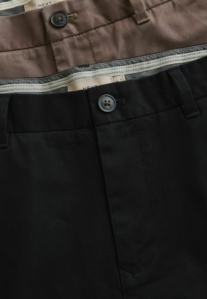 Dvi sulankstytų kelnių poros, viena juoda, kita ruda, rodančios sagstomas liemens juostas ir vidines etiketes su "NEXT" prekės ženklu.