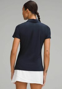 Mornarica polo majica s kratkim rukavima, teksturirana tkanina, zakrivljeni rub i ovratnik. Nositi uz bijelu plisiranu suknju, uz vidljive tetovaže.