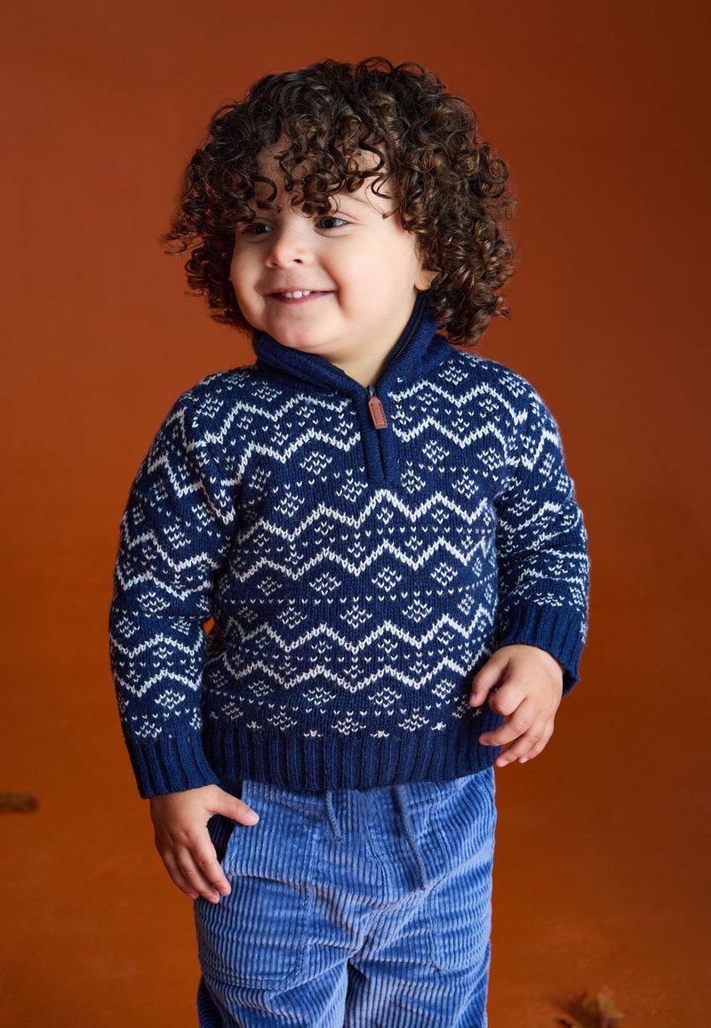 Navyblauwe gebreide trui met een wit zigzagpatroon, met een ritssluiting bij de hals. Gepaard met lichtblauwe corduroy broek.