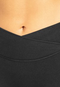 Pantaloncini sportivi neri con una vita ampia e a coste con un design incrociato, texture liscia e una vestibilità aderente attorno alla zona mediana.