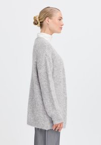 Maglione grigio in maglia fuzzy con una vestibilità rilassata, spalle scese e maniche lunghe. Presenta un colletto a coste e un retro leggermente allungato.