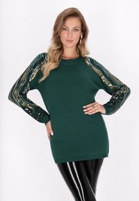 Pulover verde tricotat cu mâneci texturate și cu model, decorate cu paiete aurii și argintii. Asortat cu leggingi negri lucioși.