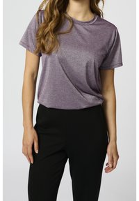 Lila glittrig t-shirt med korta ärmar och avslappnad passform, i kombination med svarta tajta byxor, vilket skapar en enkel, modern look.