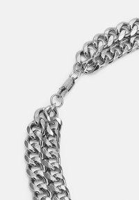 Colar de corrente em metal prateado com elos interligados, apresentando uma textura suave e fecho de engate.