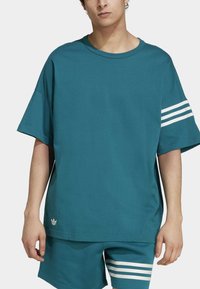 Teal oversized t-särk, millel on ümar kaelus, lühikesed varrukad ja kolm valget triipu vasakul varrukal. Esitatud koos vastava lühikeste pükstega.