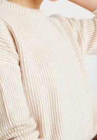 Sweter w paski w kolorze kremowym i beżowym, z prążkowaną fakturą, z okrągłym dekoltem i długimi rękawami. Miękka, lekka tkanina.