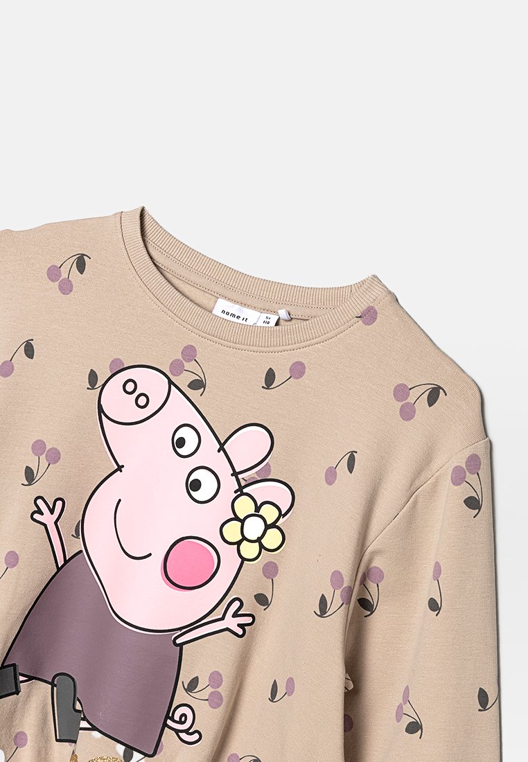 Helles beiges Sweatshirt mit einem Cartoon-Schweine-Graphic, kurzen Ärmeln und einem Rundhalsausschnitt. Dekoriert mit lila Beerenmustern.