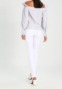 Blusa a hombros descubiertos con rayas, mangas abullonadas, puños abotonados y cintura ajustada, combinada con jeans skinny blancos y tacones blancos.