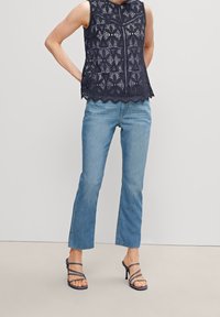 Navy Spitzen-Ärmeloses Oberteil mit gewelltem Saum, kombiniert mit hellblauen Jeans und gestreiften marineblauen Absätzen. Glatte Textur und ausgeklügelte Details sichtbar.