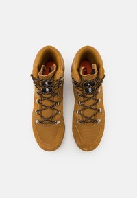 Brown hiking shoes with suede and mesh materials, featuring black and orange laces, metal hardware, and a high-top design for ankle support.