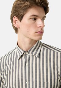 Overhemd met knopen, verticale grijze en crèmekleurige strepen, kraagontwerp en een borstzak. Heeft een glad, geweven textuur en klassieke knopen.