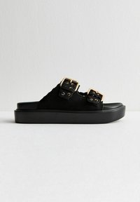 Sandales à glissière en daim noir avec deux larges brides et boucles dorées, présentant une semelle épaisse en plateforme noire et un dessus texturé.