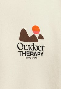 Crème katoen stof heeft een ontwerp met bruine bergen en een zon icoon in een gradient van oranje en roze. De tekst luidt "Outdoor THERAPY REVOLUTION."