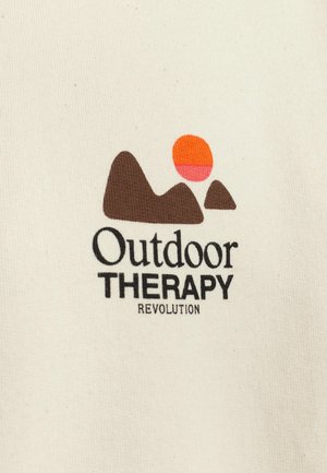 Cremefarbene Baumwollstoffe zeigen ein Design mit braunen Bergen und einem Farbverlauf-Sonnenikon in Orange und Pink. Der Text lautet "Outdoor THERAPIE REVOLUTION."