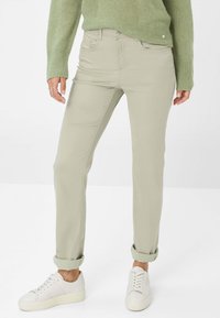 Chino en coton vert clair avec une coupe droite, ourlets roulés, poches avant et une texture lisse, associés à des baskets blanches.