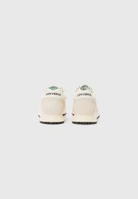 Tenisi albi cu finisaj din piele în suede, având o talpă de cauciuc neagră, formă rotundă și logo-ul "CONVERSE" pe călcâi.