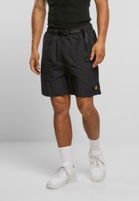 Svarte nylonshorts med elastisk midjebånd og justerbar snor. Har en liten gul logo på den nederste kanten. Kombineres med hvite joggesko.