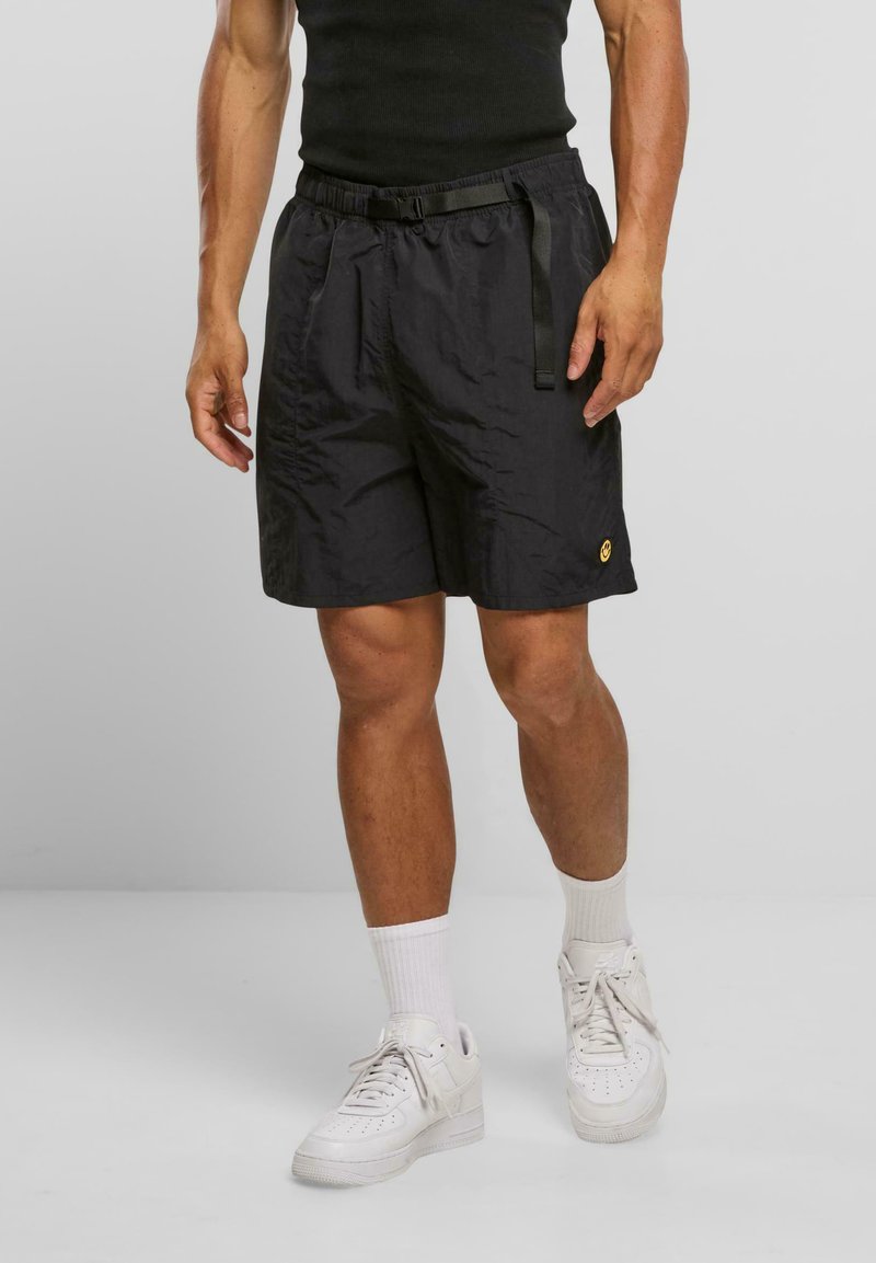 Svarte nylonshorts med elastisk midjebånd og justerbar snor. Har en liten gul logo på den nederste kanten. Kombineres med hvite joggesko.