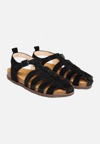 Schwarze Wildledersandalen mit mehreren breiten Riemen, offenem Zehenbereich, verstellbarem Knöchelriemen und einer strukturierten braunen Sohle.