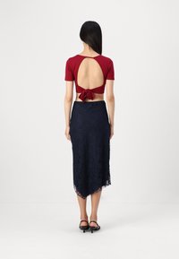 Κόκκινο κοντομάνικο crop top με ανοιχτή πλάτη, δεμένο στη μέση. Συνδυασμένο με μια ναυτική δαντελένια midi φούστα με οδοντωτή άκρη. Μαύρες γόβες.