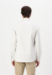 Camisa de manga longa bege clara com finas riscas verticais, colarinho com botões e bainha curva. Tecido suave com punhos e detalhes em botão.