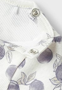 Vêtement à col avec un tissu léger, présentant un motif de fruits violets. Fermeture à boutons-pression, fond texturé blanc avec des rayures.