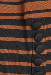 Randig tröja med svarta och orange horisontella ränder, ribbat mönster och stora svarta knappar på sidan.