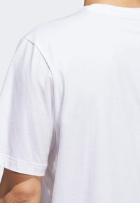 Camiseta blanca de algodón con mangas cortas, cuello redondo y textura suave, mostrando la vista trasera y los detalles de la costura del hombro.