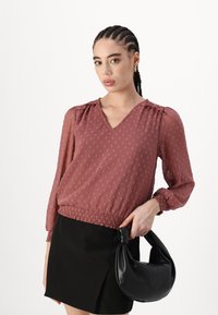 Blusa rosa con pois in rilievo, scollo a V, maniche gatherate e vita elastica, abbinata a una mini gonna nera e a una borsa nera.