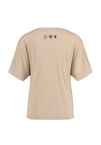 Camiseta de manga corta beige en tejido suave, con un corte holgado y tres pequeños corazones oscuros impresos en la parte superior de la espalda.