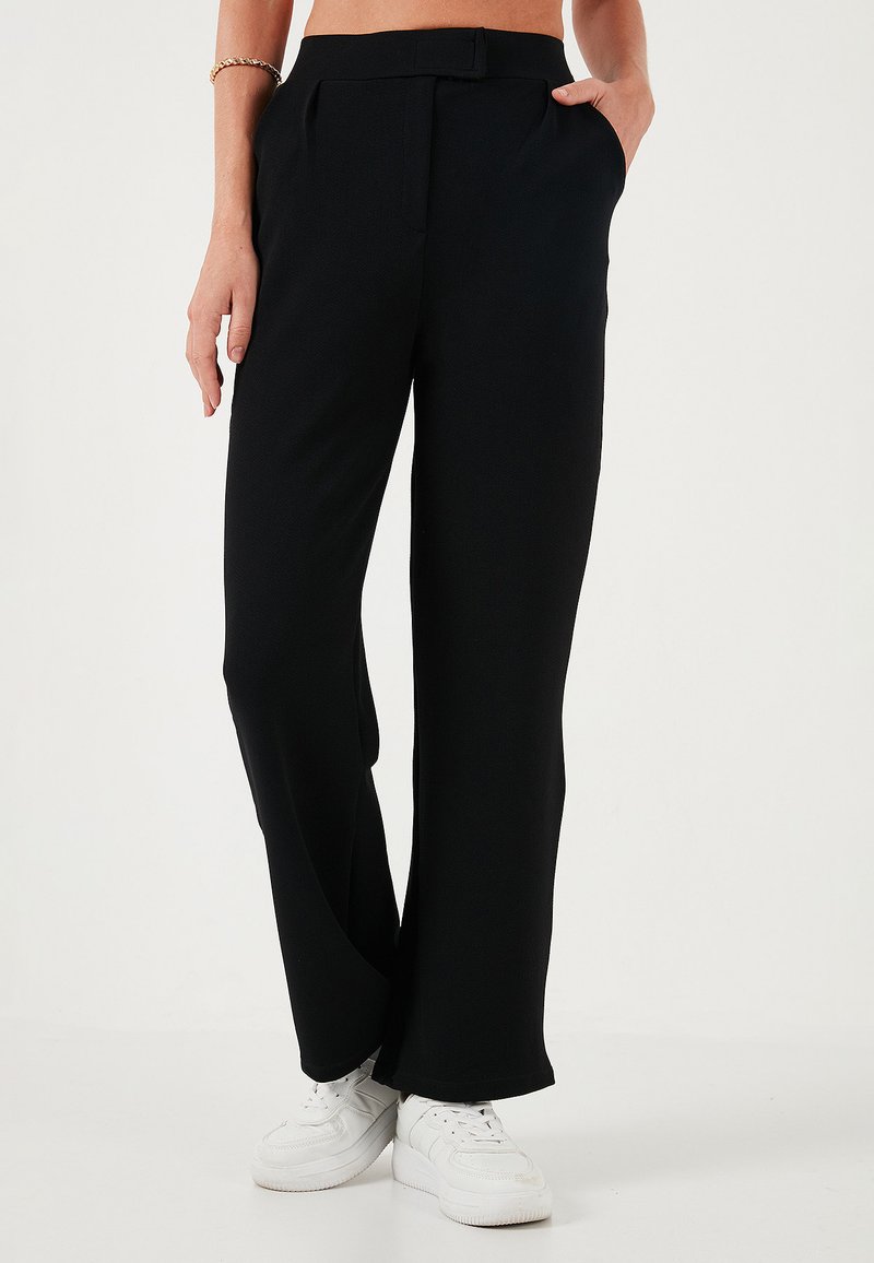 Zwarte, wijde pantalons met een gladde textuur, geplooide voorkant en zijzakken. Draagt het met witte sneakers voor contrast.