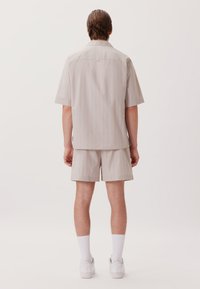 Chemise à manches courtes gris clair et short assorti avec des fines rayures bleues, en tissu lisse, associés à des chaussettes sportives blanches et des chaussures.