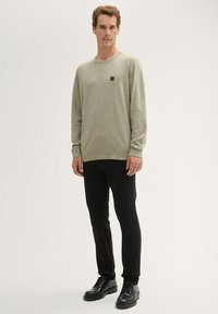 Jasnozielona koszula z długim rękawem, okrągłym dekoltem i małym logo. Połączona z czarnymi spodniami slim fit i czarnymi sznurowanymi butami.