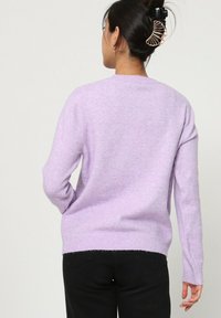 Pull violet clair à manches longues en matière douce. Doté d'un col rond et d'un ourlet côtelé. Porté avec un jean noir, vu de dos.