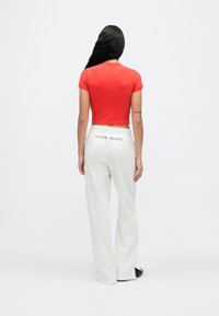 Κόκκινο κοντομάνικο crop top σε συνδυασμό με ανοιχτό γκρι φόρμα, με το κείμενο "NIKE SHOX" στην πλάτη, φορεμένο με μαύρα παπούτσια τύπου slip-on.