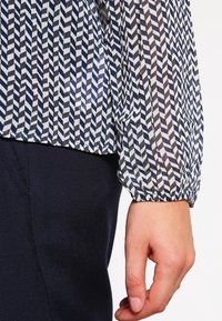 Blusa a righe blu e bianca con design a zig-zag, tessuto leggero, maniche arricciate e vestibilità comoda.