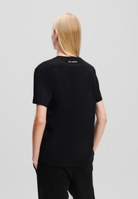 Juodas marškinėliai, pagaminti iš lygaus medvilnės, su trumpomis rankovėmis ir apykakle. Ant nugaros pakeistas "KARL LAGERFELD" logotipas.