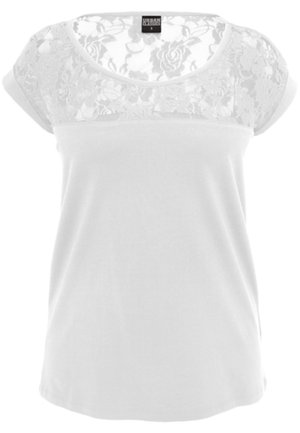 Blusa blanca de manga corta con patrón floral de encaje en el pecho y los hombros, tela lisa debajo.