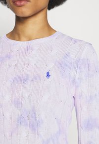 Jasnofioletowy sweter z grubym splotem wykonany z bawełny. Posiada okrągły dekolt oraz małe haftowane logo na lewej piersi.