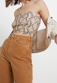 Haut sans bretelles imprimé serpent beige associé à un jean en denim taille haute de couleur brun clair. Le haut présente une texture lisse et un design ajusté.