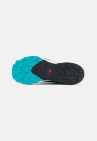 Sole di scarpa da corsa nera e teal, dotata di un motivo di battistrada robusto con tacchetti pronunciati, superfici testurizzate e un accento rosso al centro.